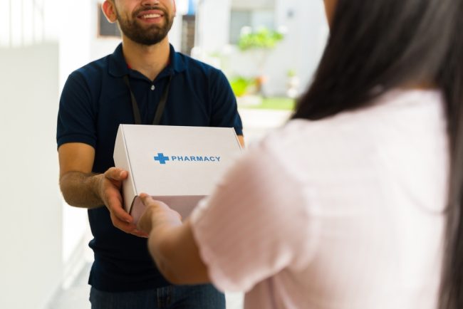 Smiling,Delivery,Man,Holding,A,White,Box,With,The,Word Healthcare Delivery Service
