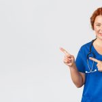 Medicine, healthcare and coronavirus concept. Portrait of pleasant female doctor, redhead nurse in blue scrubs looking upbeat, showing clinic banner, hospital advertisement, pointing finger left.